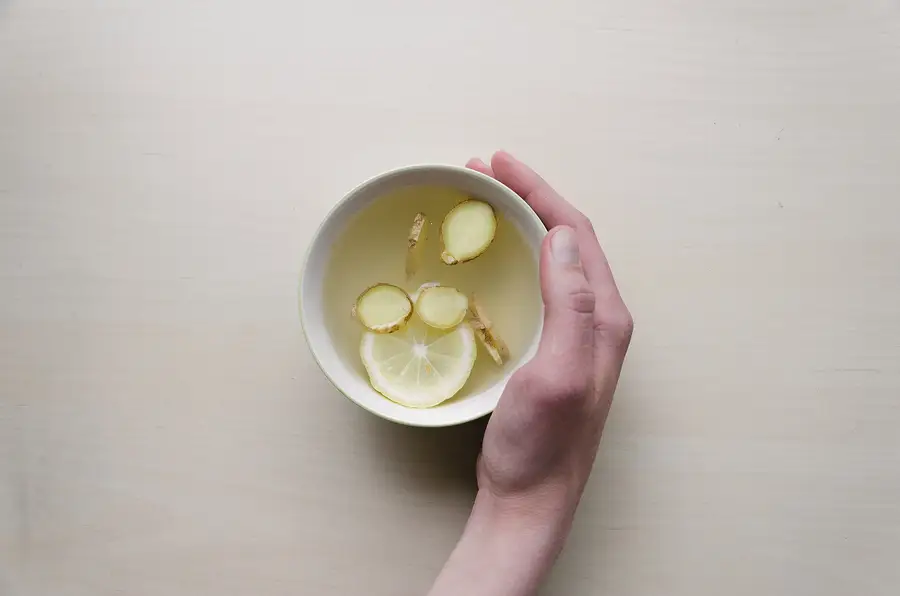 A hand holding a bowl of warm ginger and lemon detox drink